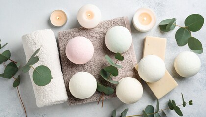 Top view of spa essentials including bath bombs, candles, eucalyptus leaves, towels, and soap bars arranged on a light background for a relaxing atmosphere.