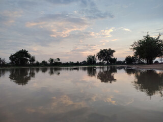 Obraz premium A serene and tranquil landscape scene captured at dusk or dawn, featuring a calm body of water perfectly reflecting the soft colors of the sky and the silhouettes of distant trees.