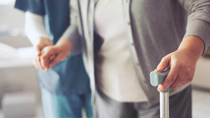 The nurse is helping the old patient with a cane