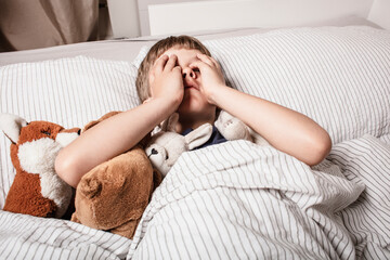 The boy was scared before going to bed. Night terrors in a child. The kid covers his face with his hands in a fear. Children's experiences. Boy in the bed. View from above. Sad psychological state.