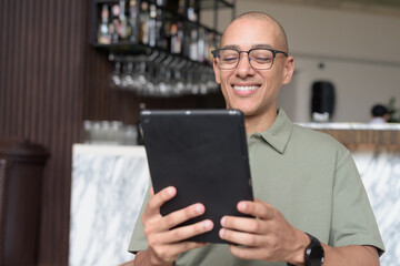 Latin adult man using tablet computer in hotel lounge or bar, travel lifestyle and technology focus