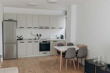 Compact kitchen interior with integrated appliances, matte cabinetry, and neutral color palette. Dining area for four highlights functionality and style.Modern light kitchen with wooden floor, dining 