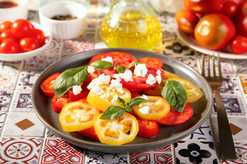 Sliced fresh tomato salad with basil leaves sprinkled with feta cheese