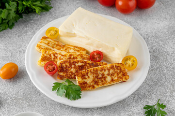 Fried and raw halloumi cheese on a white plate on a gray concrete background.