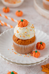 Pumpkin spice cupcakes decorated butter cream frosting, sugar sprinkles and mini sweet pumpkins on top. Thanksgiving or Halloween dessert.