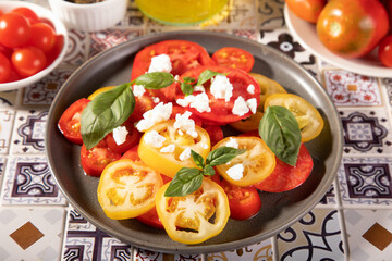 Sliced fresh tomato salad with basil leaves sprinkled with feta cheese