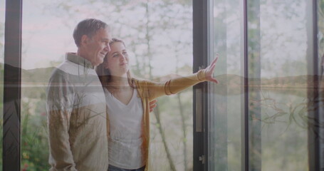 Pointing granddaughter in cardigan guiding grandfather to wooded view home, near sliding glass door