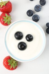 Tasty yoghurt with blueberries and strawberries in bowl on white table, flat lay