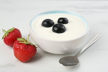 Tasty yoghurt with blueberries and strawberries in bowl on white marble table, closeup