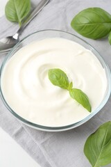 Tasty yoghurt with basil in bowl on white table, closeup