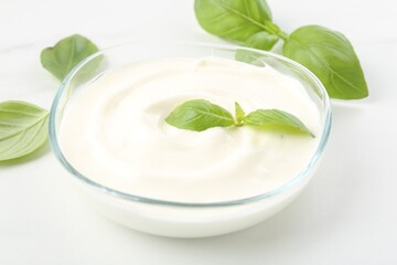 Tasty yoghurt with basil in bowl on white table, closeup