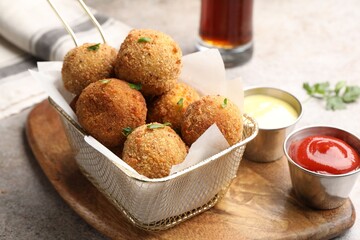 Delicious fried croquette balls with parsley and sauces on grey textured table, closeup