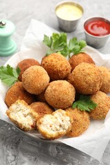Delicious fried croquette balls with parsley in bowl on grey textured table, closeup