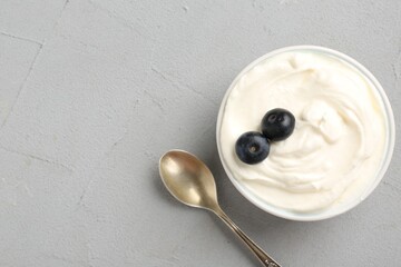 Delicious yogurt in bowl, blueberries and spoon on grey table, flat lay. Space for text