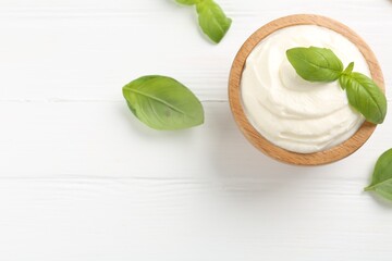 Delicious yogurt in bowl and basil on white wooden table, flat lay. Space for text