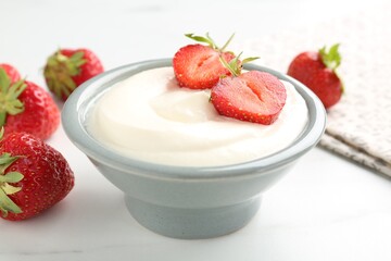 Delicious yogurt in bowl and strawberries on white marble table, closeup