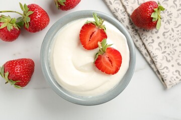 Delicious yogurt in bowl and strawberries on white marble table, flat lay