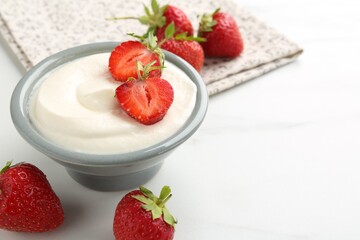 Delicious yogurt in bowl and strawberries on white marble table, closeup. Space for text