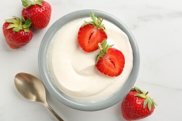 Delicious yogurt in bowl, strawberries and spoon on white marble table, flat lay