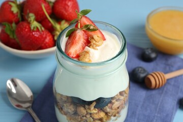 Tasty yogurt with granola, berries and honey on light blue table, closeup