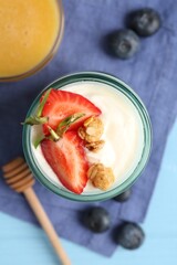 Tasty yogurt with granola, berries and honey on light blue table, flat lay