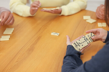 Obraz premium Friends playing dominoes at wooden table, closeup