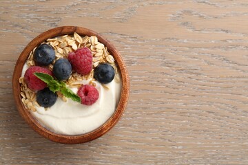 Tasty yogurt with granola and berries in bowl on wooden table, top view. Space for text
