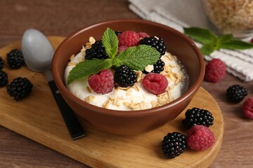 Tasty yogurt with granola and berries in bowl on wooden table, closeup