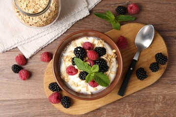 Tasty yogurt with granola and berries in bowl on wooden table, flat lay