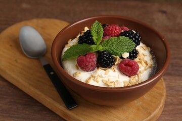 Tasty yogurt with granola and berries in bowl on wooden table, closeup