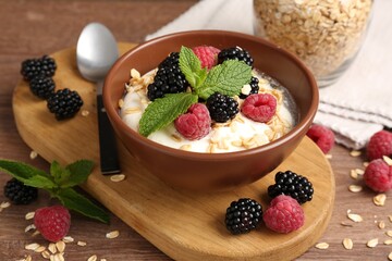 Tasty yogurt with granola and berries in bowl on wooden table, closeup