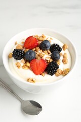 Tasty yogurt with granola and berries in bowl on white marble table, closeup
