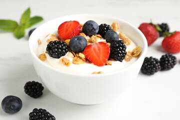 Tasty yogurt with granola and berries in bowl on white table, closeup