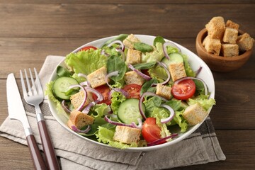 Delicious salad with croutons and vegetables served on wooden table, closeup