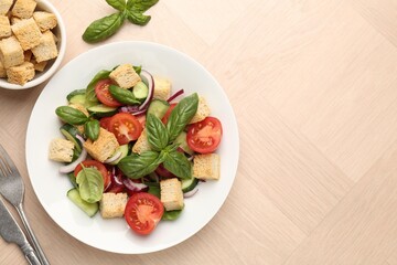 Delicious salad with croutons, vegetables and basil on wooden table, flat lay. Space for text