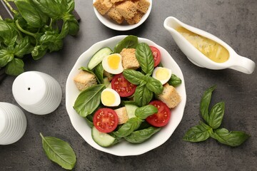 Tasty salad with croutons, tomatoes, cucumbers and basil on black table, flat lay