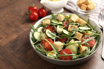Tasty salad with croutons, cucumbers, tomatoes and arugula on wooden table, closeup. Space for text