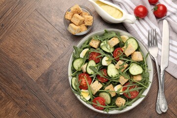 Tasty salad with croutons, cucumbers, tomatoes and arugula on wooden table, flat lay. Space for text