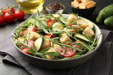 Tasty salad with croutons, cucumbers, tomatoes and arugula on black table, closeup
