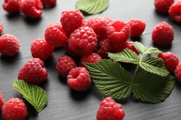 Tasty fresh ripe raspberries and leaves on black table, closeup