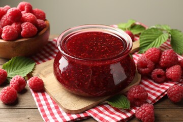Tasty jam, fresh ripe raspberries and leaves on wooden table, closeup.
