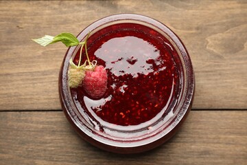 Tasty raspberry jam in glass jar on wooden table, top view