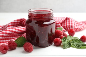 Tasty jam, fresh ripe raspberries and leaves on white wooden table, closeup