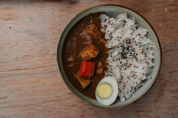 A bowl of Japanese curry with rice and a soft-boiled egg sits on a wooden table.