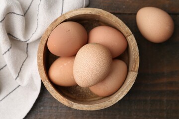 Raw chicken eggs in bowl on wooden table, top view