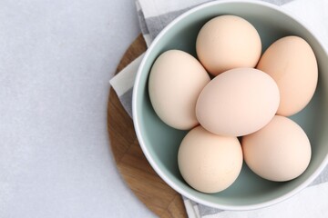 Raw chicken eggs in bowl on white table, top view. Space for text