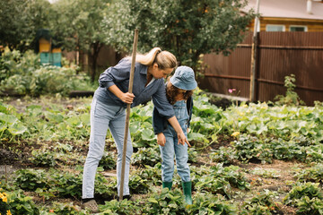 Happy family mom, girl and teenager boy working in a garden with rake and shovel. Countryside farm.
