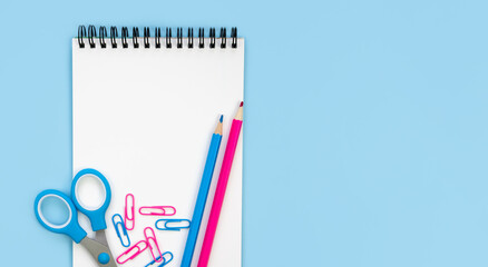 Notebook, pencils, scissors and paperclips on a blue background. Back to school. Flatlay. Top view. Copy space.