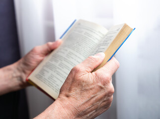 Fototapeta premium Senior man reads book. The pensioner is resting at home. Close-up. Selective focus.