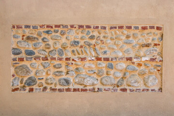 Light brown plastered wall with red brick inserts in rows and large river stones cemented in exposed view. Graphic element for background and texture, copy space.